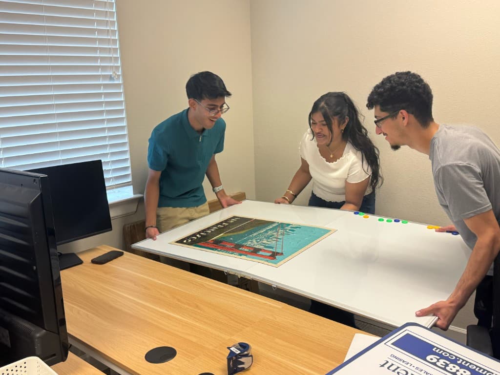 Three interns holding a whiteboard with a San Francisco poster during a working session